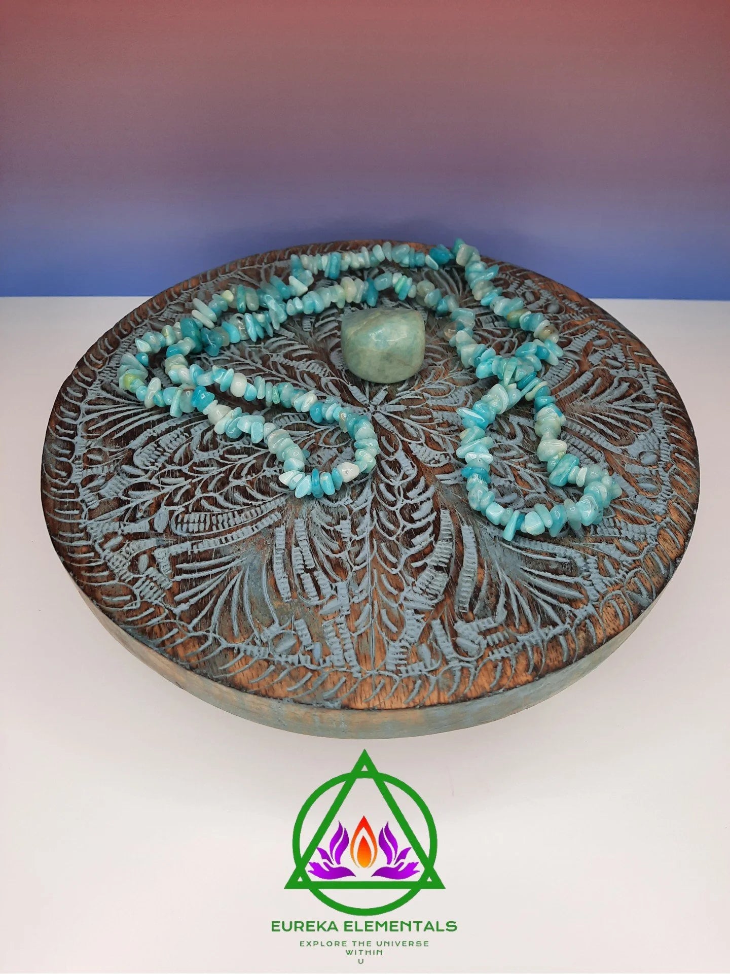 Amazonite Necklace and Crystal resting on a wooden stand with a red and blue ombre backdrop.