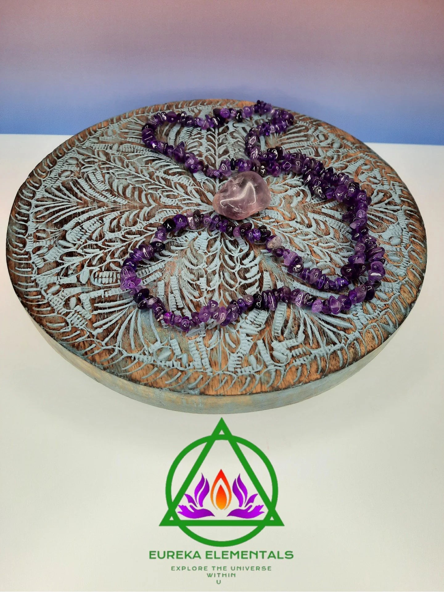 Amethyst Necklace and Crystal resting on a wooden stand with a red and blue ombre backdrop. 