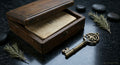 Wooden box with tarot cards within it with sage on its sides and a key in front of it resting on a black marble countertop. 