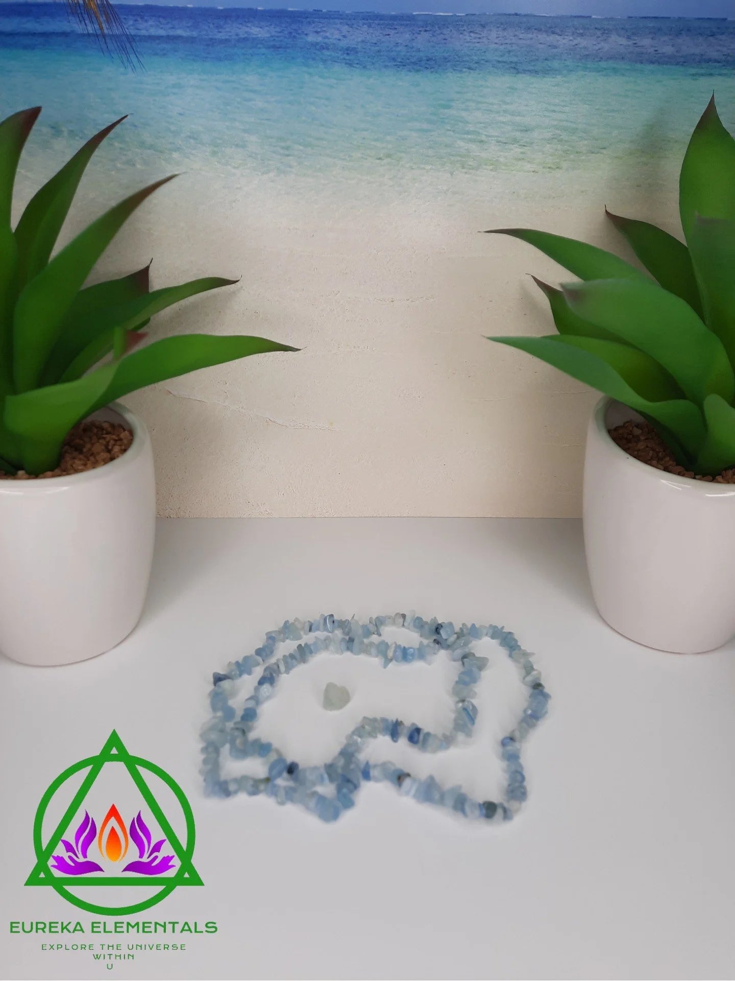 Aquamarine Necklace and Blue Topaz Crystal resting between two planters with a beach background. 