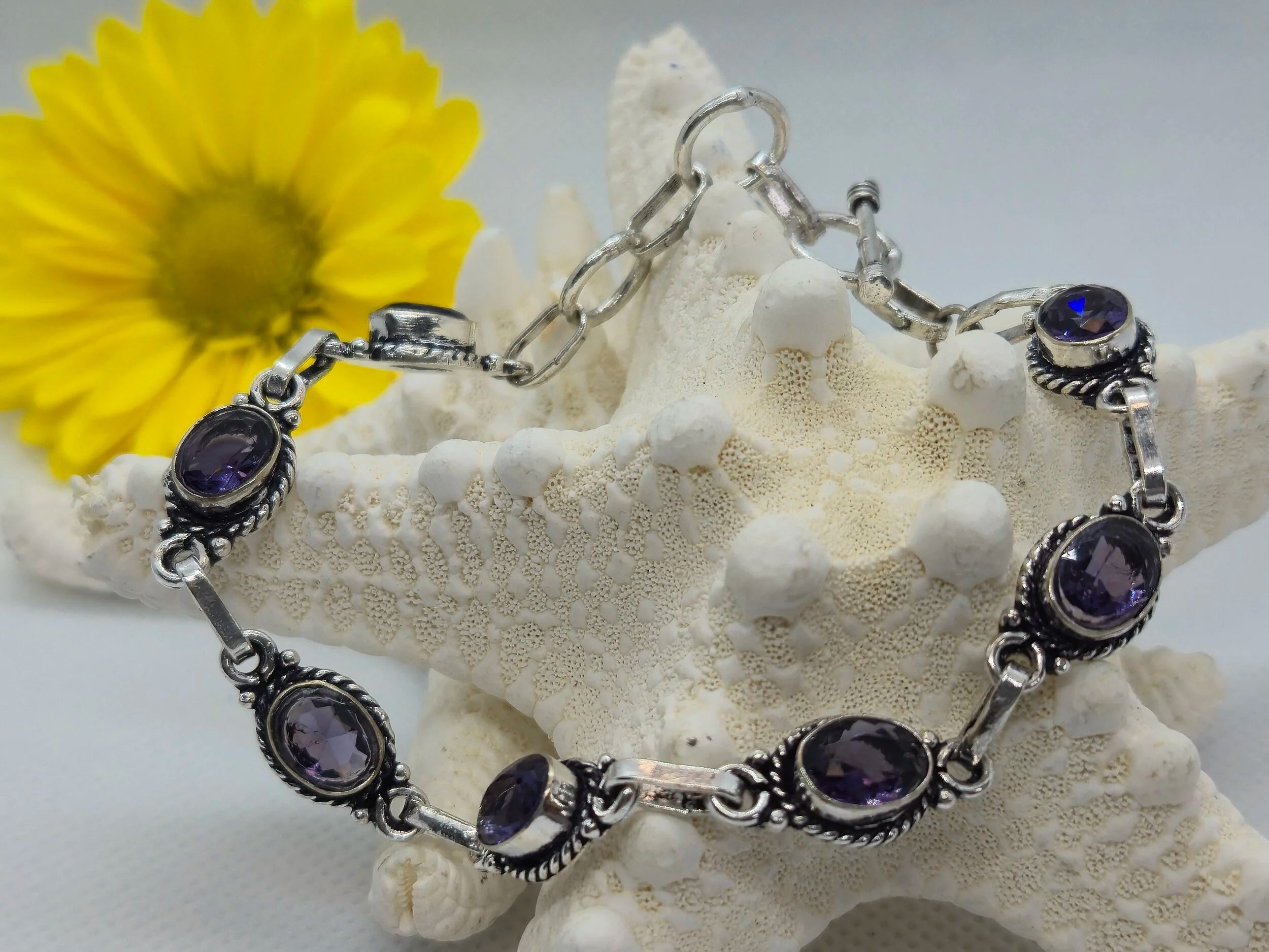 One Artisan Amethyst Silver Toggle Bracelet wrapped around a white starfish with a sunflower in the largely white background. 