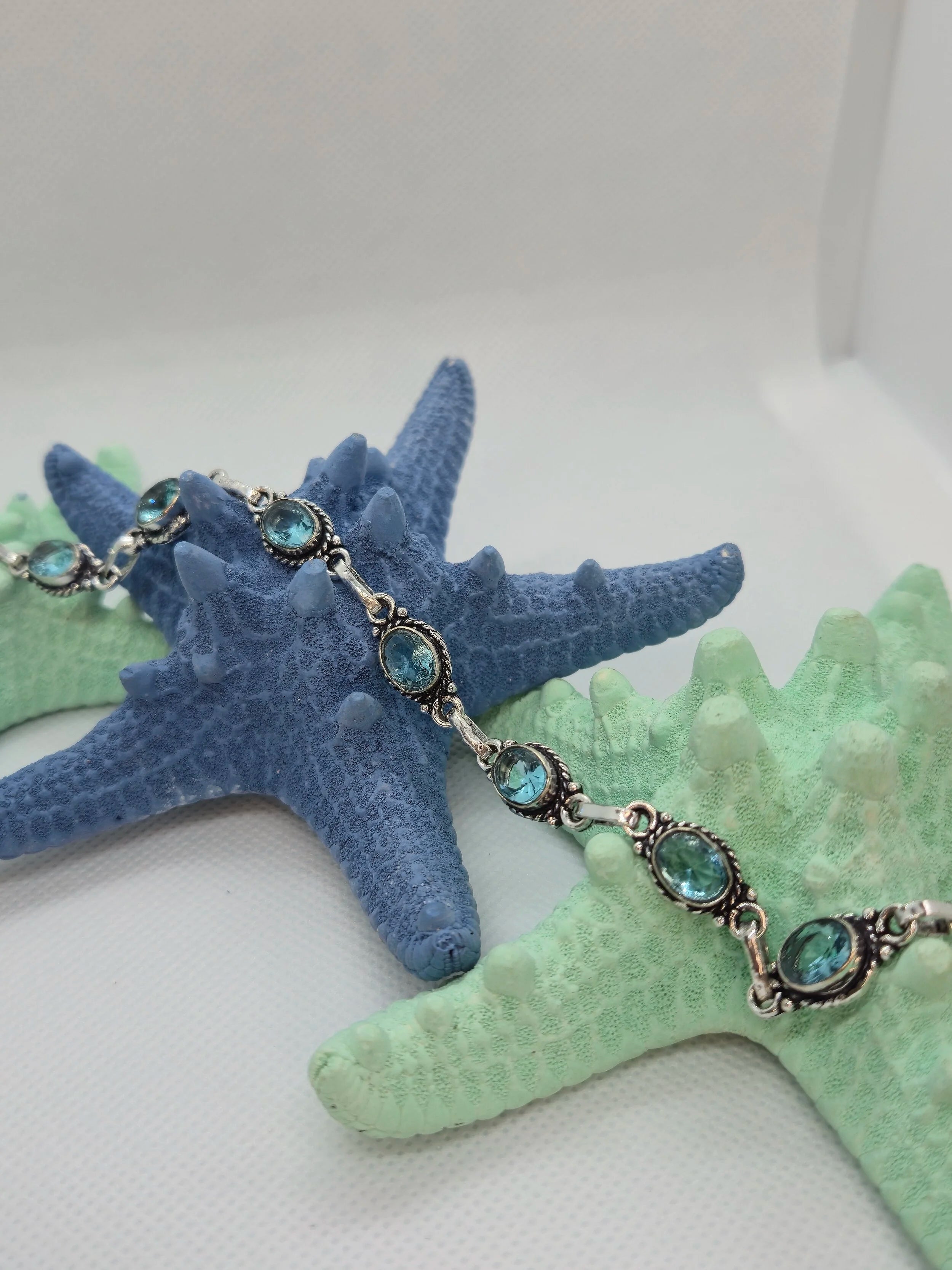 One Artisan Blue Topaz Silver Toggle Bracelet laid over a single navy starfish and two aquamarine starfishes with a white background. 