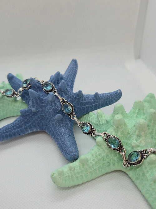One Artisan Blue Topaz Silver Toggle Bracelet laid over a single navy starfish and two aquamarine starfishes with a white background. 