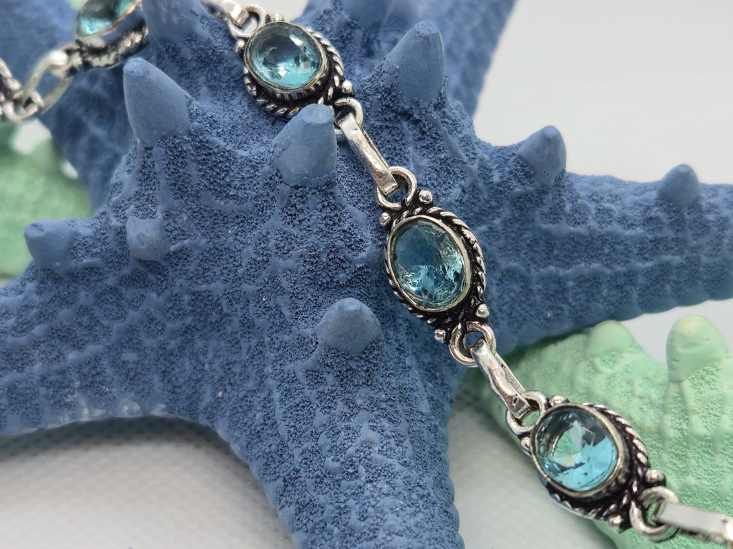One Artisan Blue Topaz Silver Toggle Bracelet laid over a single navy starfish at an up close view. 