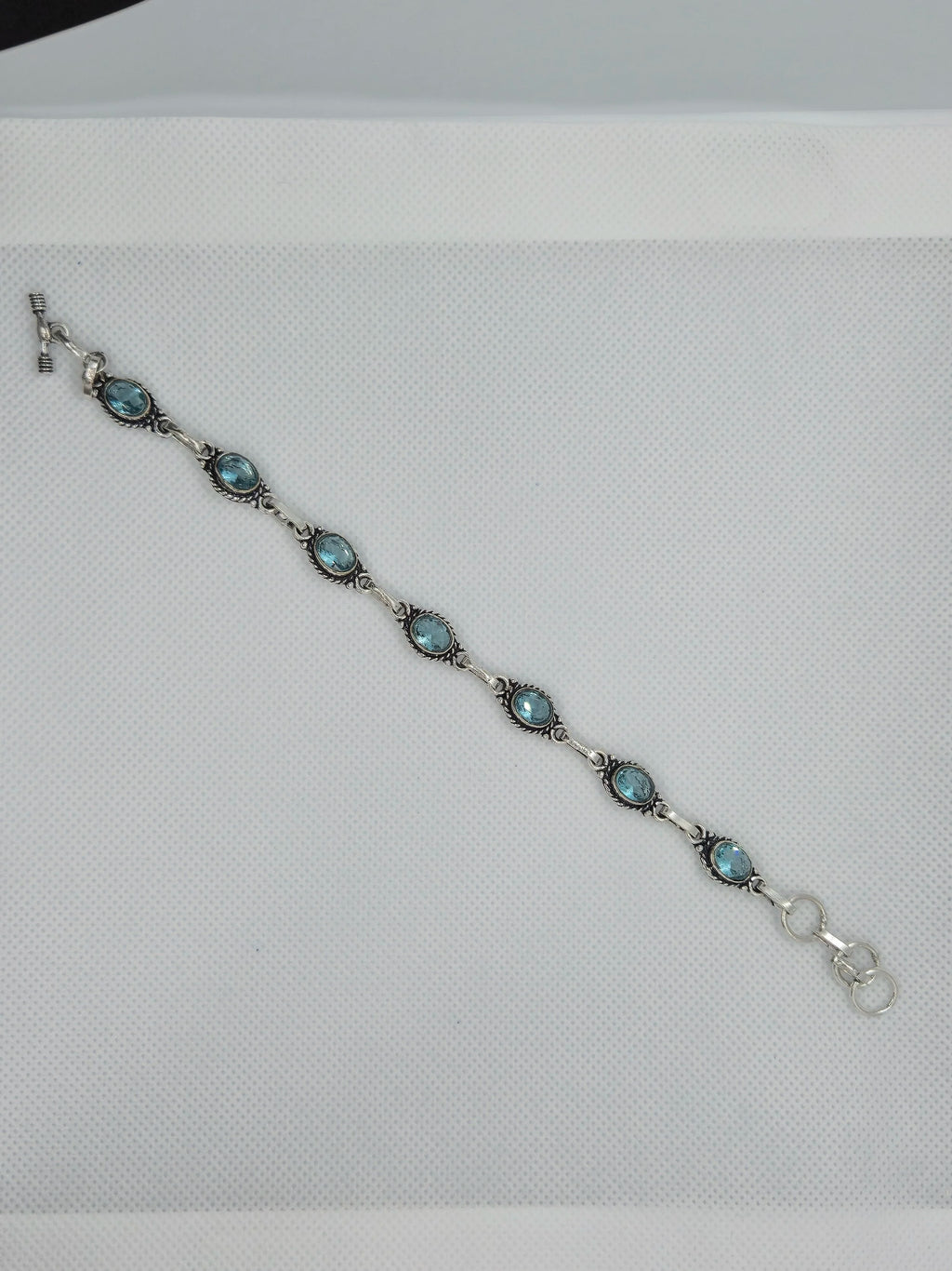 One Artisan Blue Topaz Silver Toggle Bracelet laid over a white cloth background. 