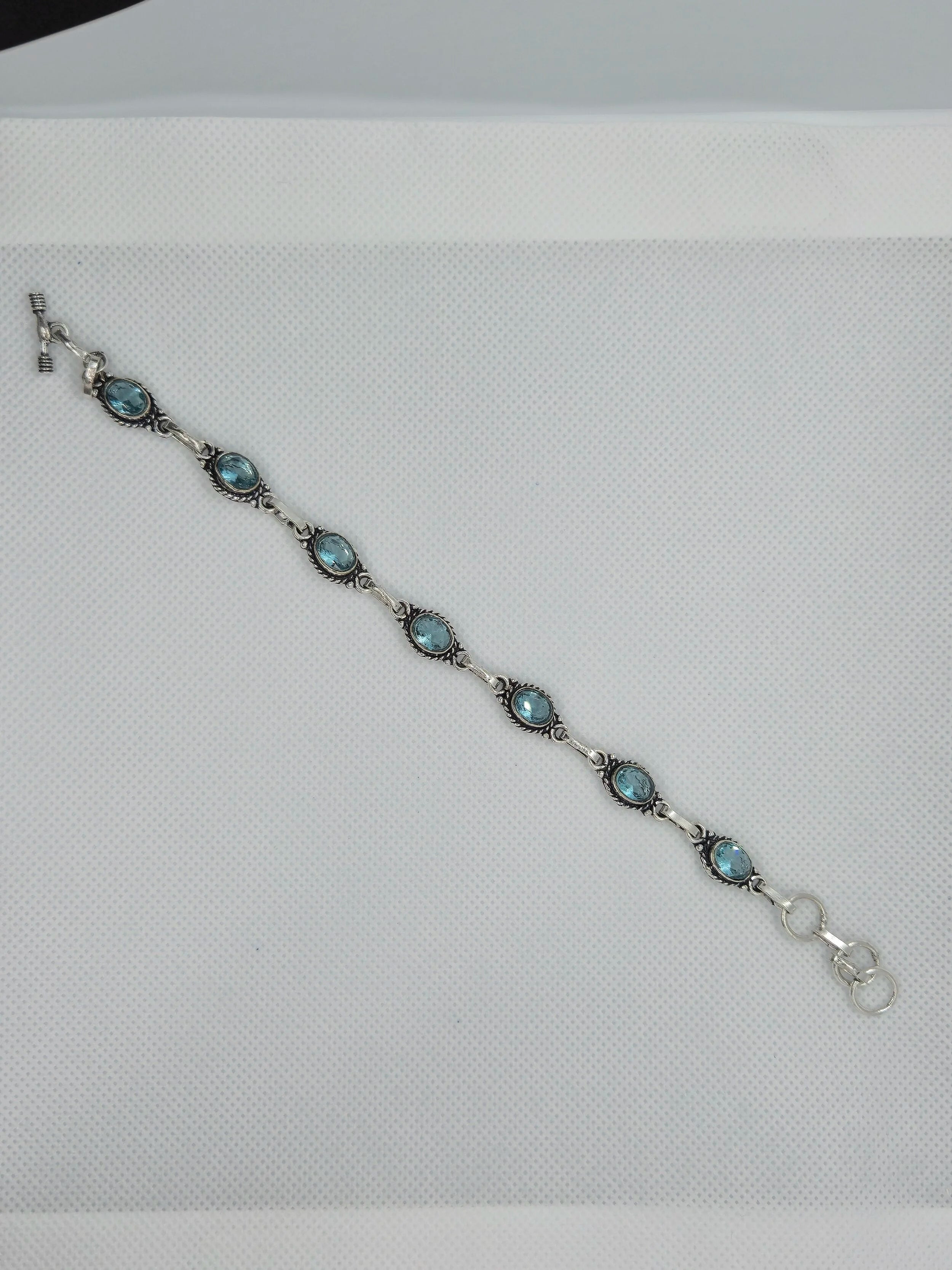 One Artisan Blue Topaz Silver Toggle Bracelet laid over a white cloth background. 