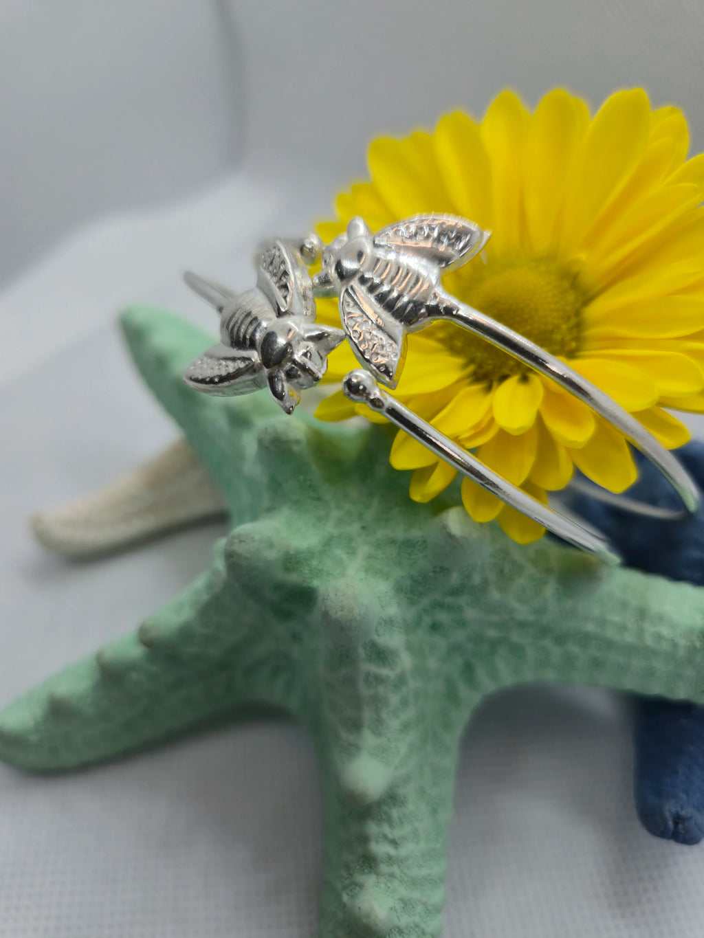 Two Artisan Silver Bumble Bee Bangles with an aquamarine, navy, and yellow starfish in the background. 