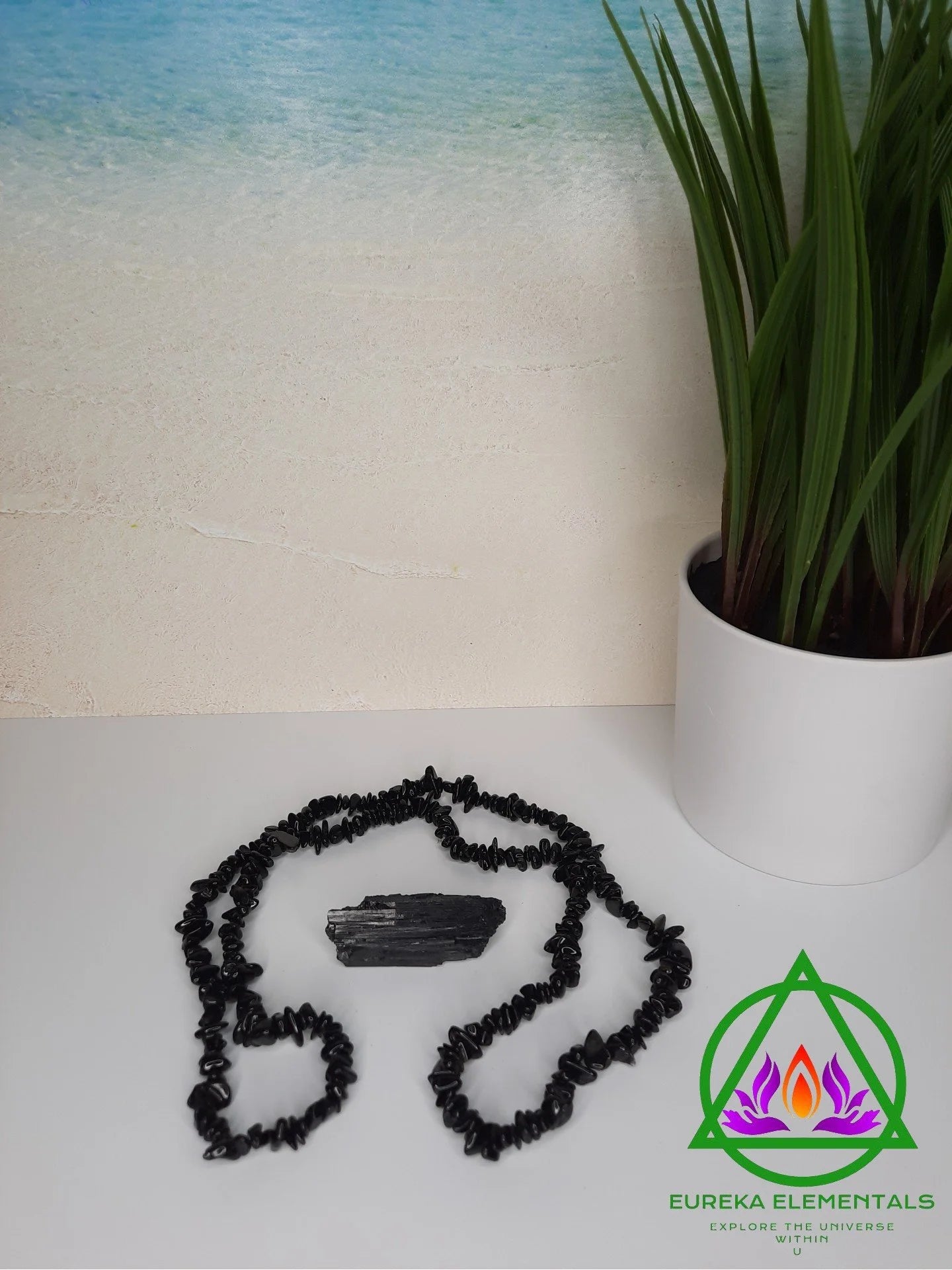Black Tourmaline Necklace and Crystal resting on a white foreground with a sea water backdrop. 