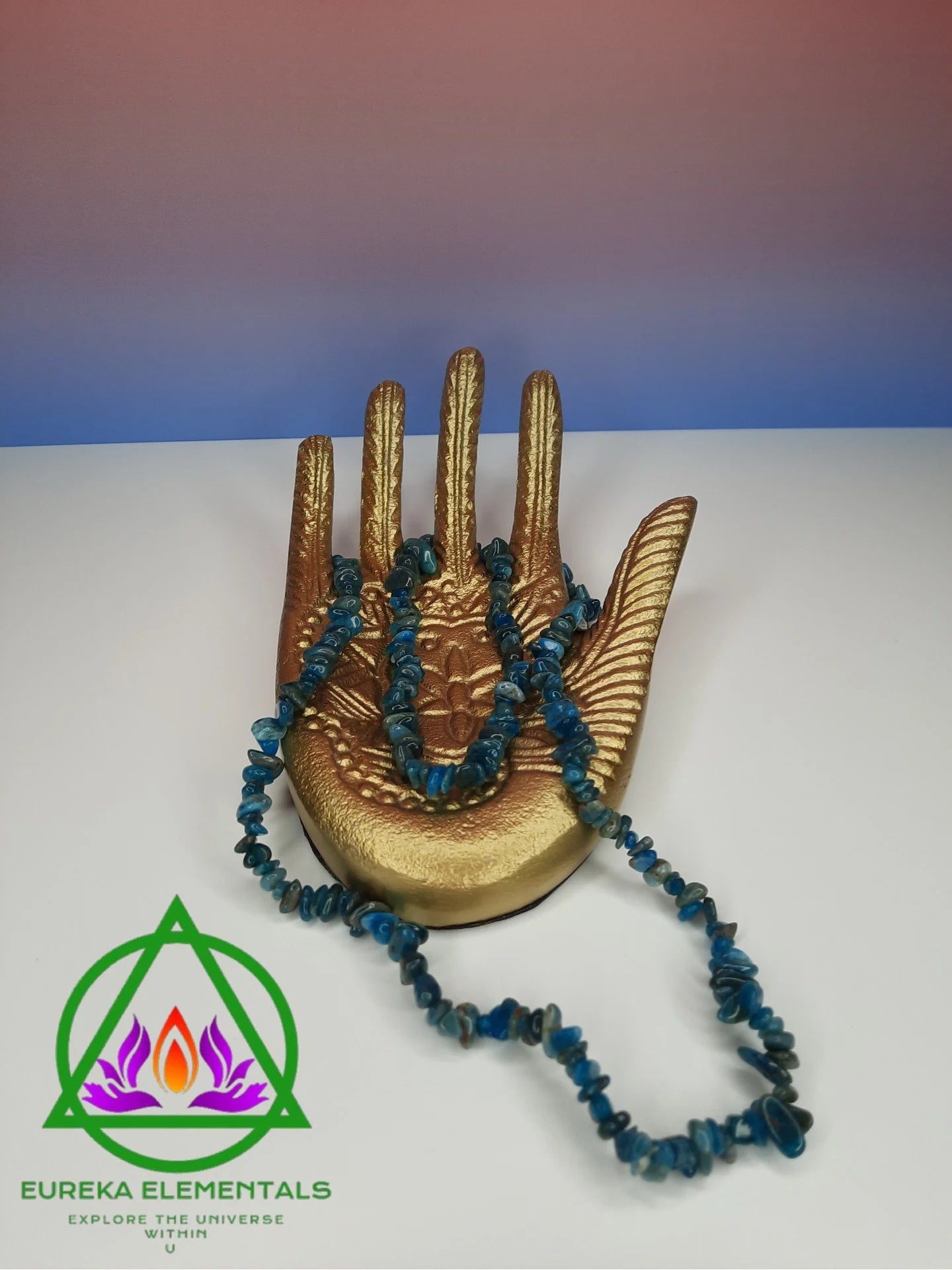 Blue Apatite Necklace resting on a golden hand with a red and blue ombre background. 