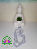 Blue Chalcedony Necklace and Blue Quartz Crystal resting next to a ceramic Buddhist statue with a beach background