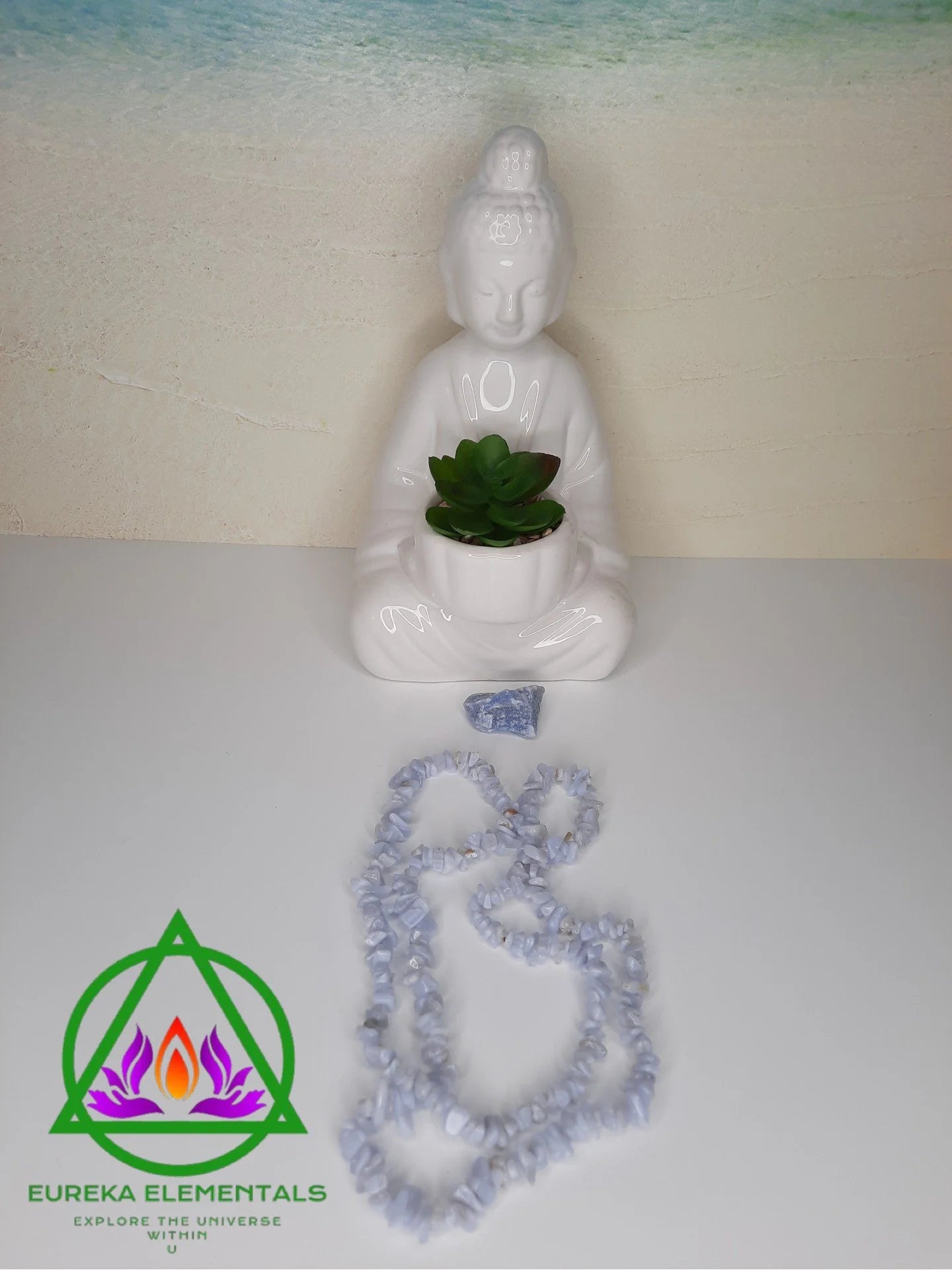 Blue Chalcedony Necklace and Blue Quartz Crystal resting next to a ceramic Buddhist statue with a beach background