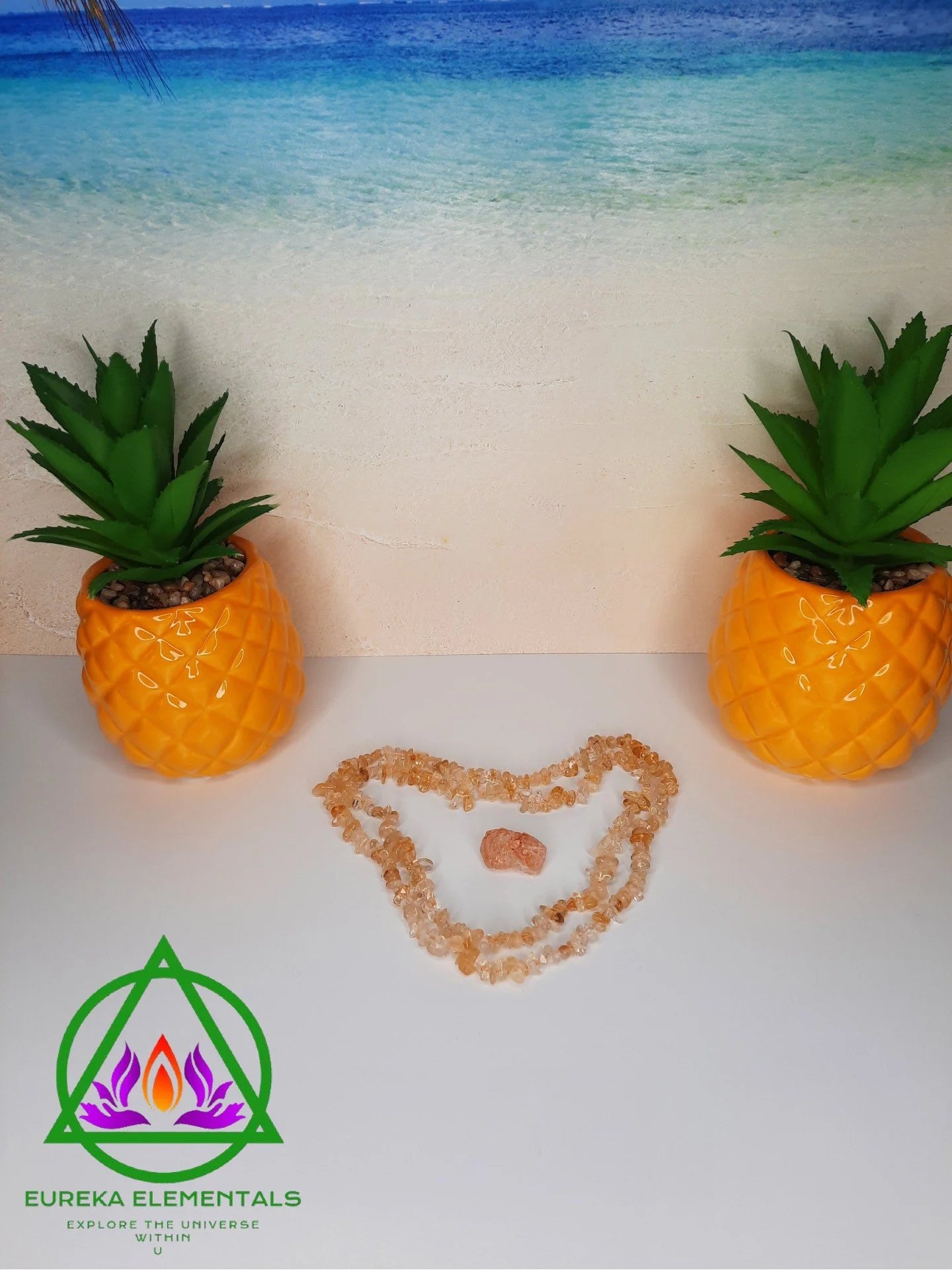 Citrine Necklace and Crystal resting between two pineapple shaped planters with a beach background.