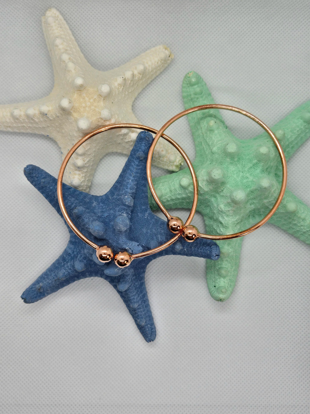 Two Heavy Copper West Indian Bangles resting on top of an aquamarine and navy starfish with a white cloth background. 