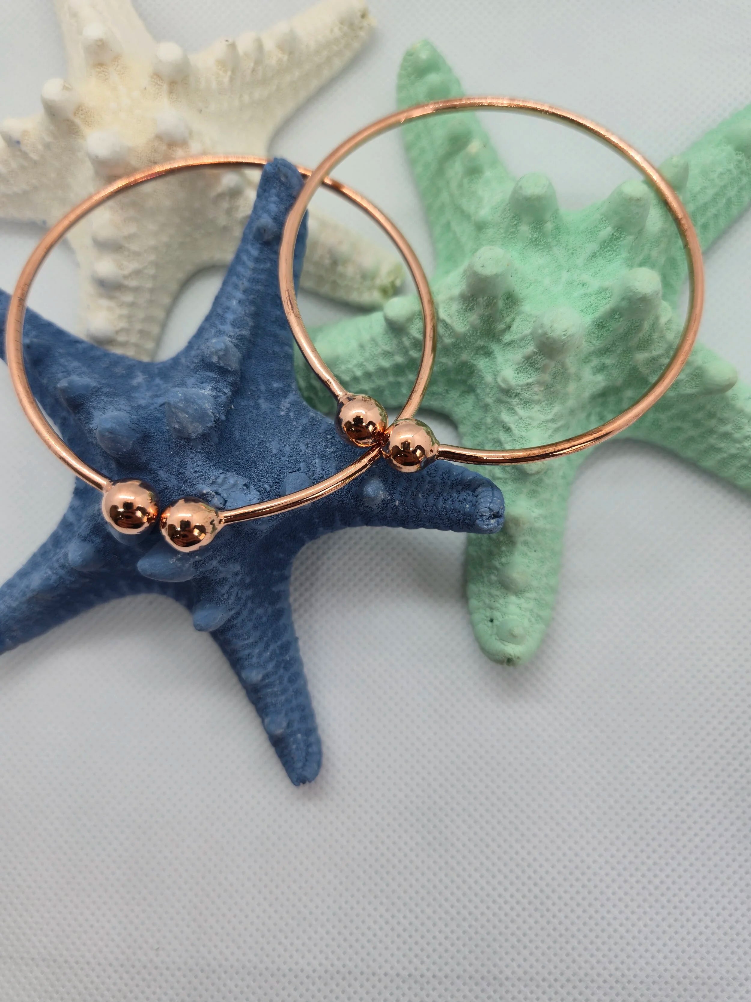 Two Heavy Copper West Indian Bangles resting on top of a aquamarine and navy starfish with a white cloth background. 