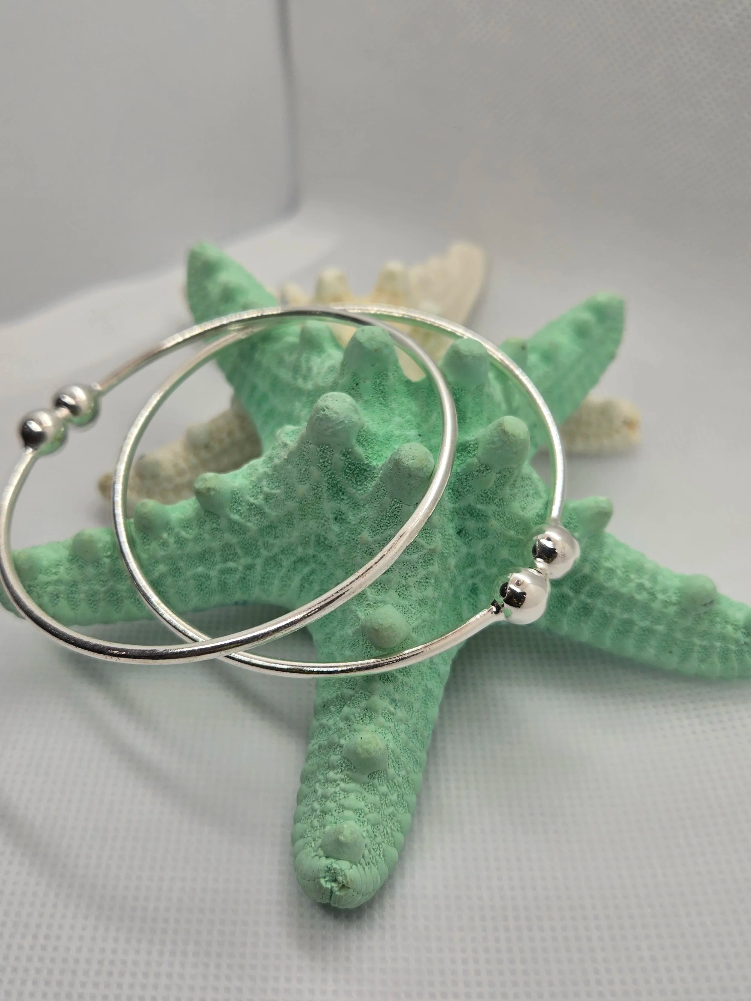Two Heavy Silver West Indian Bangles dangling off a an aquamarine starfish. 