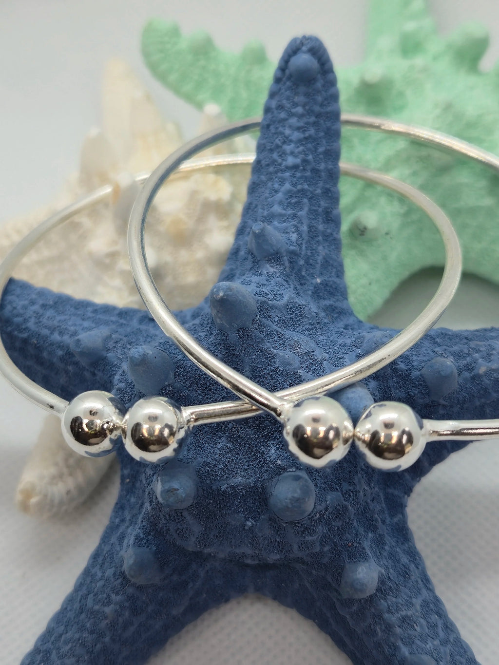 Two Heavy Silver West Indian Bangle Pairs hooked on a navy blue starfish. 