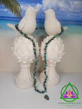 Hubei Turquoise Necklace and Crystal resting between two white dove statues with a beach backdrop.