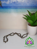Labradorite Necklace resting on a white foreground next to a potted plant with a beach background. 