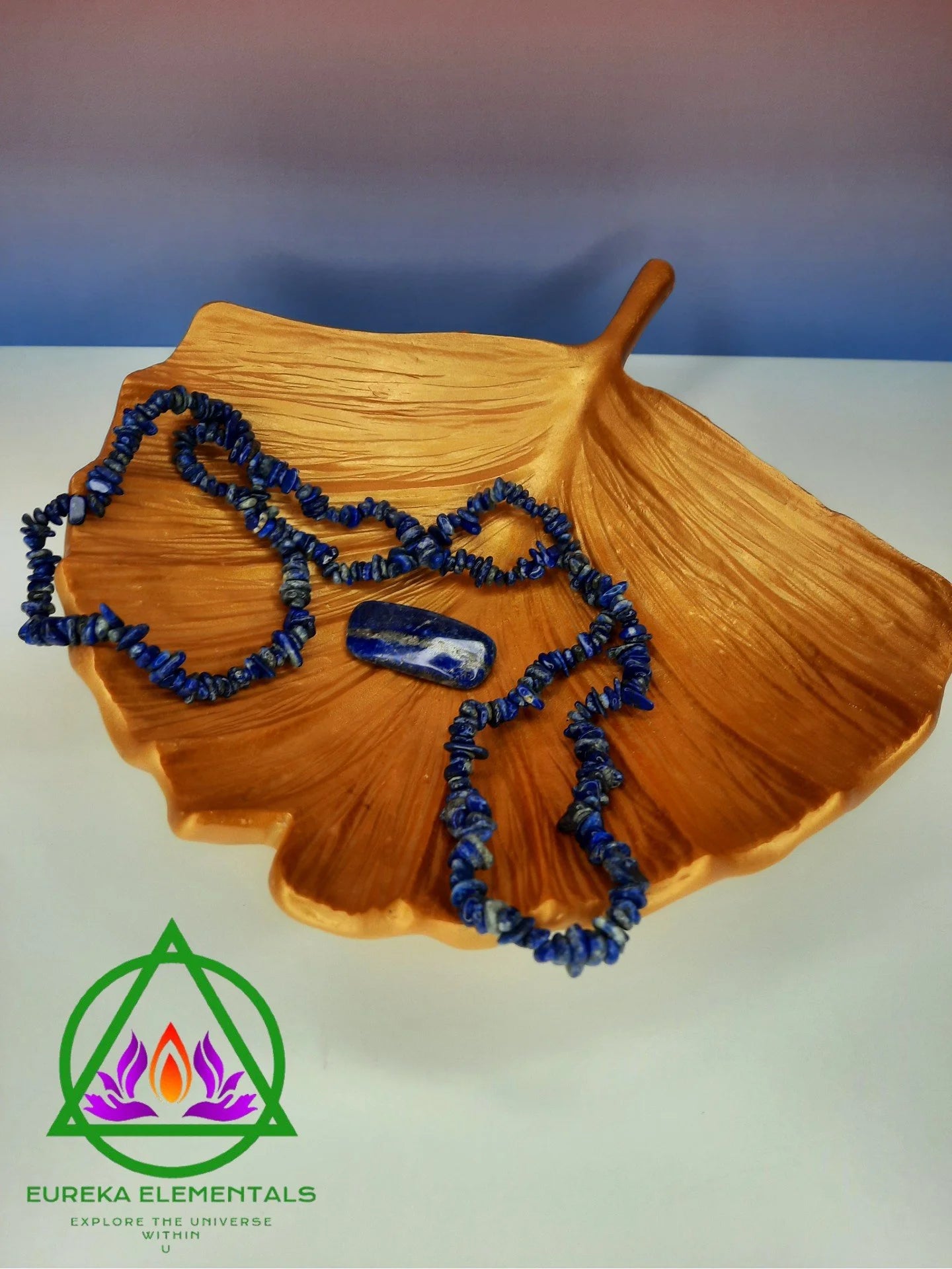 Lapis Lazuli Necklace and Crystal on a Golden Leaf with a red and blue ombre backdrop. 