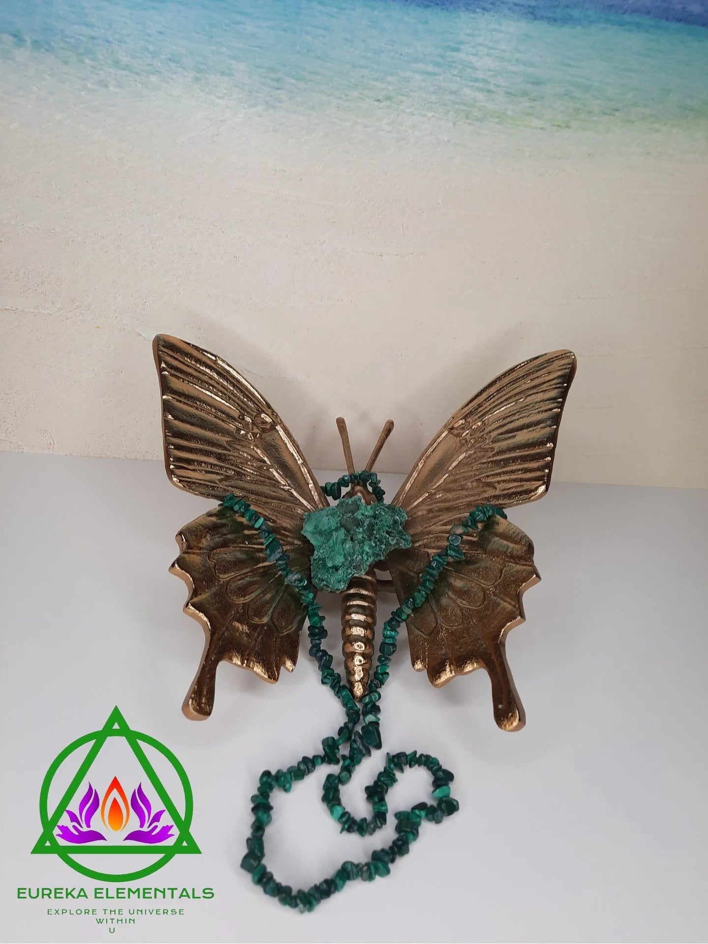 Malachite Necklace and Crystal resting on a Bronze Butterfly with a beach backdrop. 