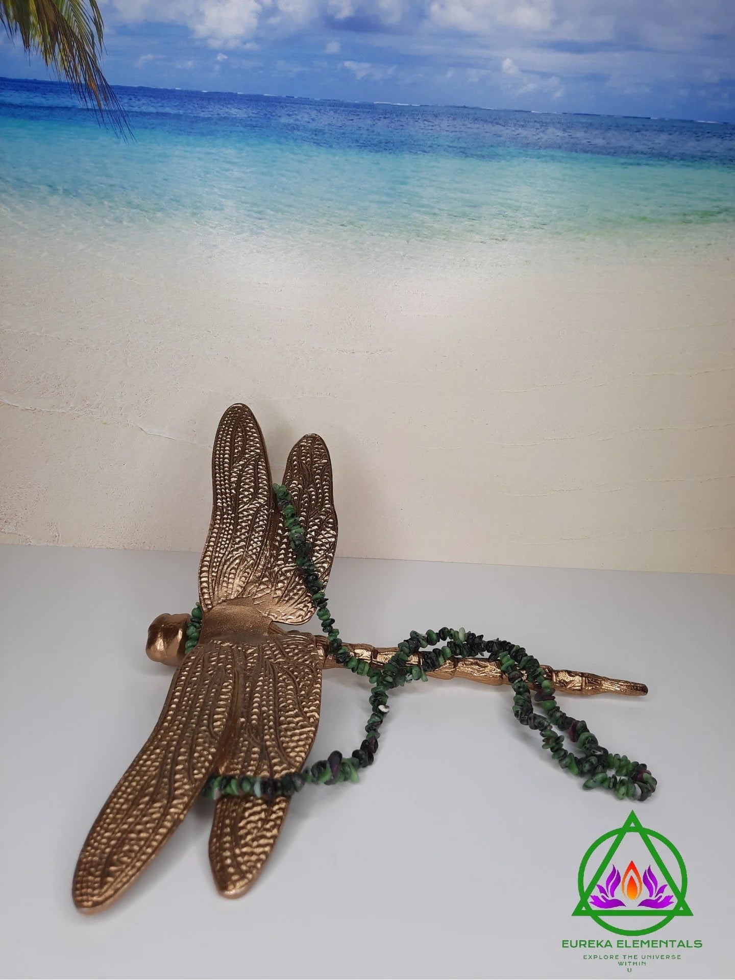 Ruby in Zoisite Necklace resting on a Bronze Dragonfly with a beach backdrop. 