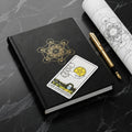 Book with the Ace of Pentacles on top of it with a pen to the book's side over a black marble background. 
