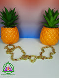Yellow Opal Necklace resting between two pineapple shaped planters with a red and blue ombre background.