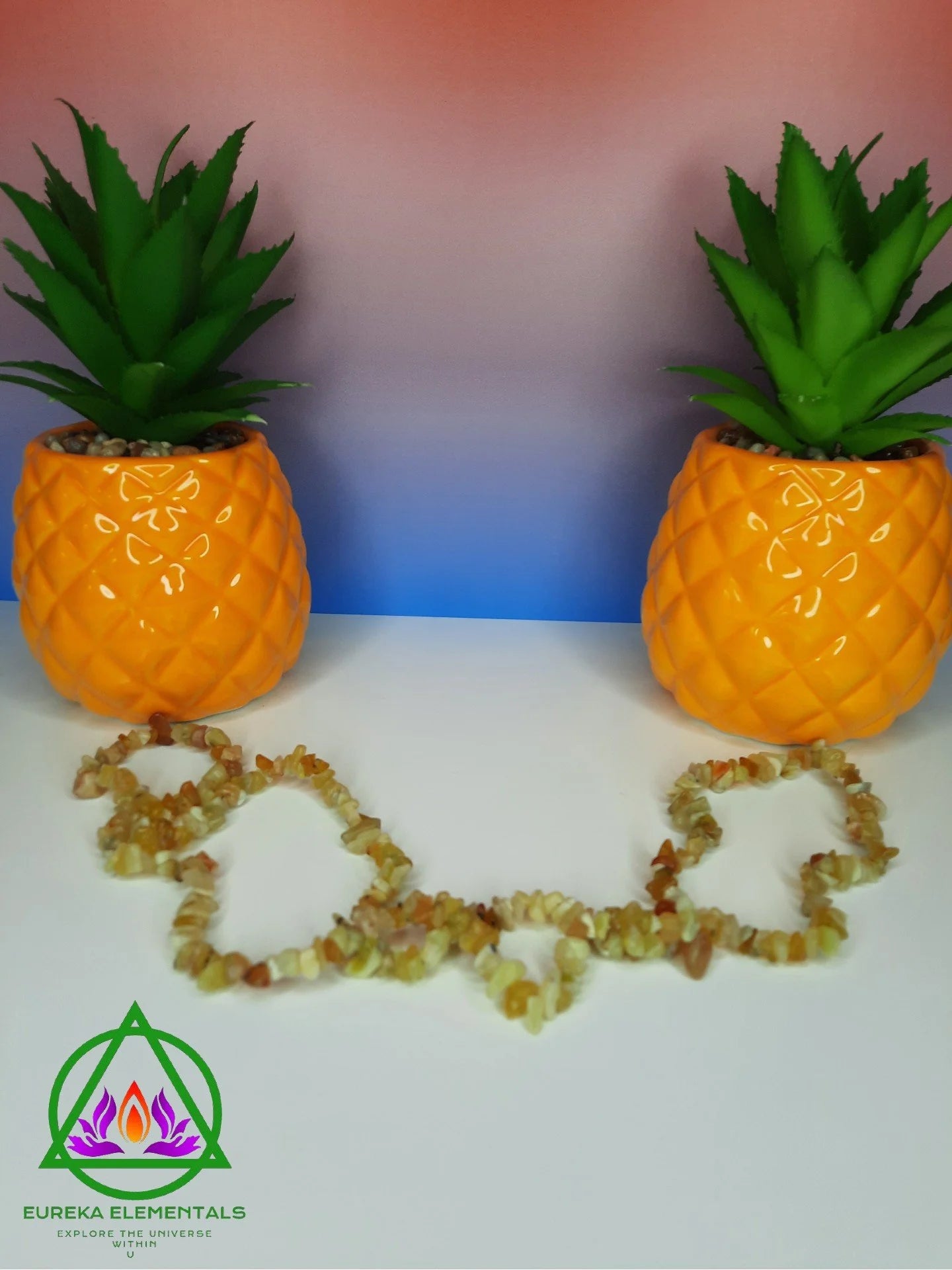Yellow Opal Necklace resting between two pineapple shaped planters with a red and blue ombre background.